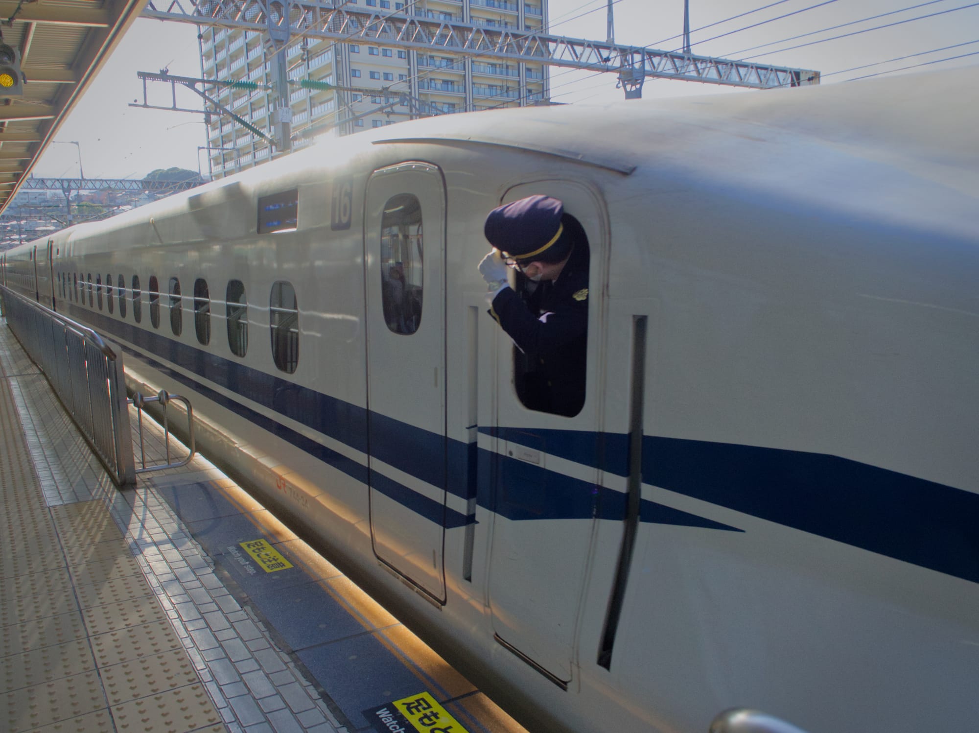 Shinkansen conductor holding onto his cap as he speeds away