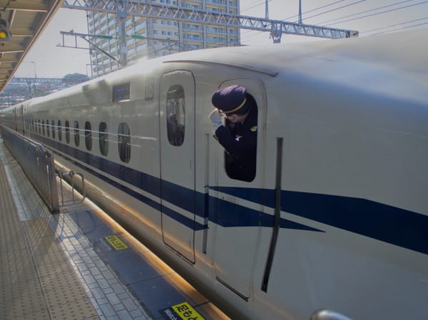 Shinkansen conductor holding onto his cap as he speeds away
